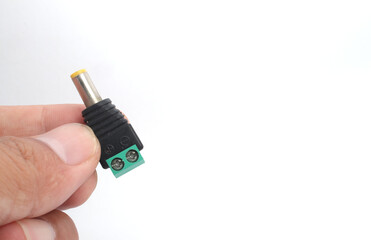 A male DC jack with green screw connection held in hand on white background.