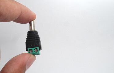 A male DC jack with green screw connection held in hand on white background.