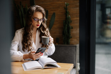 Businesswoman drinking coffee and using smartphone in cafe