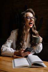 Happy businesswoman laughing while drinking coffee and using smartphone
