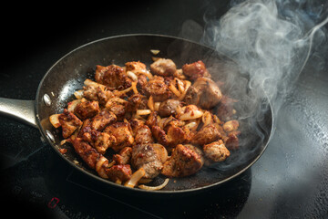 Diced pork with onions and paprika seasoning is roasted with plenty of steam in a cast iron pan on a black induction hob, cooking a meat dish like goulash, stew or ragout