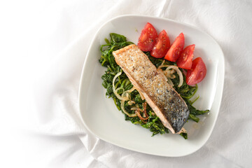 Roasted salmon fillet on with spinach vegetables with onions and tomatoes, healthy diet meal served on a white plate and tablecloth, high angle view from above, copy space