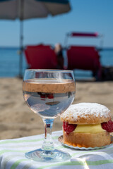 Lunch on sandy beach in Saint-Tropez with cake Tarte tropezienne filled brioche with cream and fresh red berries and glass of rose wine, summer vacation on French riviera, France