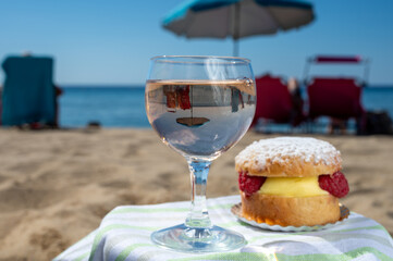 Lunch on sandy beach in Saint-Tropez with cake Tarte tropezienne filled brioche with cream and fresh red berries and glass of rose wine, summer vacation on French riviera, France