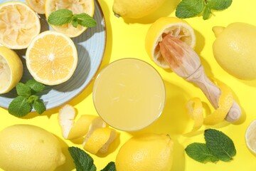 Glass of fresh lemon juice, squeezer and fruits on yellow background, flat lay