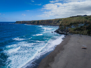 Aerial drone view of Azores islands coast with black sand beach. Praia dos Moinhos landscape in Sao Miguel, Portugal. Atlantic ocean shore with cliffs
