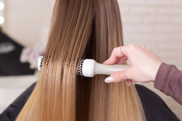 Naklejka premium Hairdresser's hand brushing long natural blonde hair in beauty salon 