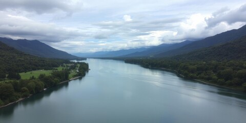 Fototapeta premium Narrow river flowing between lush greenery and tall trees, with a majestic mountain in the background under a cloudy sky, cloudy sky, tranquil