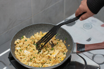 A closeup of a women hand cooking the macaroni or penne pasta in wok pan, cooking pasta homemade.