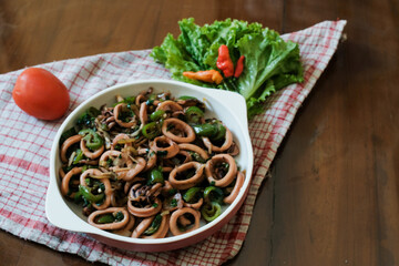 Asian food stir-fried squid vegetables with sweet soy sauce home dish, on white plate at wooden table with napkin.