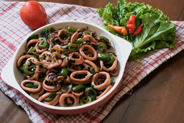 Asian food stir-fried squid vegetables with sweet soy sauce home dish, on white plate at wooden table with napkin.