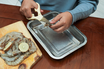 Process of hands women peel shrimps shell with scissors on the wooden table. Woman cleaning shrimp for seafood cooking