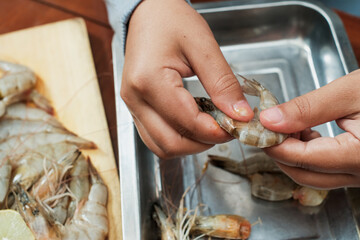 Process of hands women peel raw shrimp shell on the wooden table. Woman cleaning shrimp for seafood...