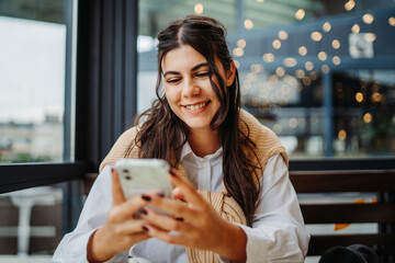 Young caucasian woman using phone in cafe to talk or send messages sms