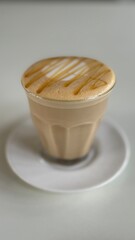 
Hot caramel macchiato in a clear glass on a white saucer served in a cafe