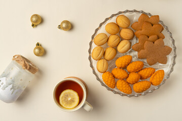 Plate with cookies, cup of tea and decoration on beige background. Flat lay, top view.