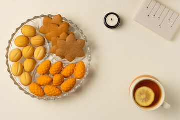 Plate with cookies, cup of tea, Christmas gift box and candle on beige background. Flat lay, top view.
