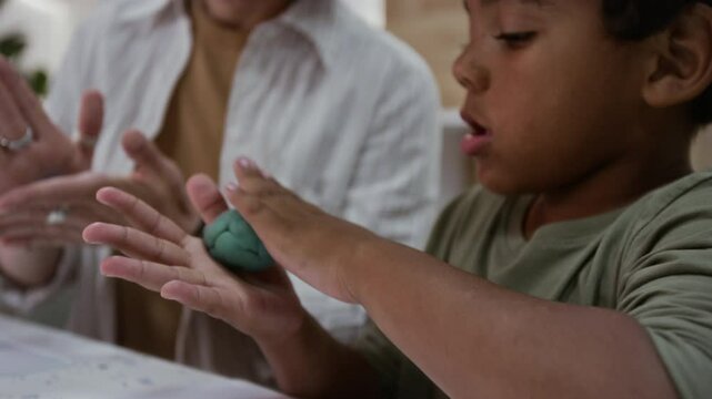 Medium close up of young African American boy sculpting from plasticine while sitting next to female teacher at group class