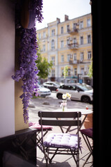 Exterior of a cafe with street furniture and decorated with wisteria near a road with cars
