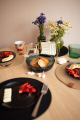 Continental breakfast wooden table with pancakes, strawberries, bananas, bouquets of wildflowers