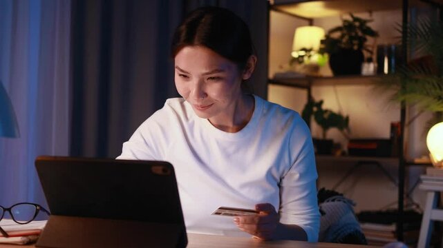 Pretty young asian woman paying with credit card on tablet computer at home Happy customer doing payments online shopping in internet store and receiving cashback at late night Easy pay concept