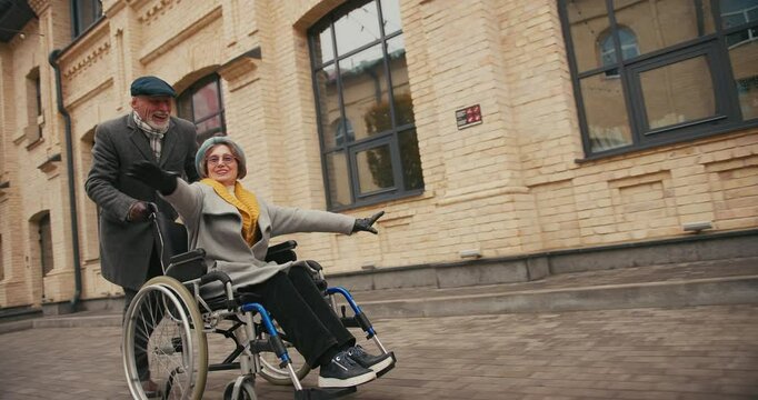 Elderly man pushes woman in wheelchair gesturing with hands