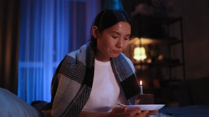 Upset asian woman in birthday party hat celebrating alone looking at cake with candle at home Pretty female feeling sad because everybody forgot about her event indoors Bad birthday mood