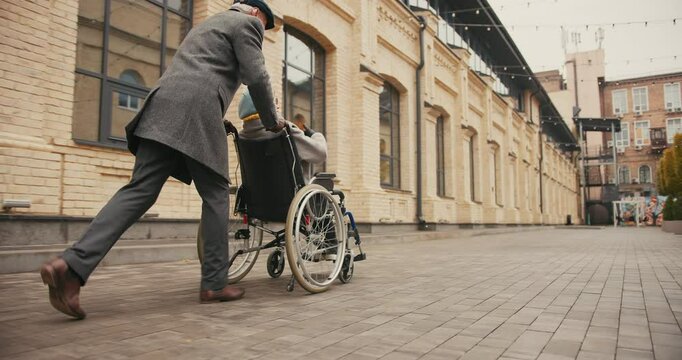 Elderly man pushes woman in wheelchair gesturing with hands