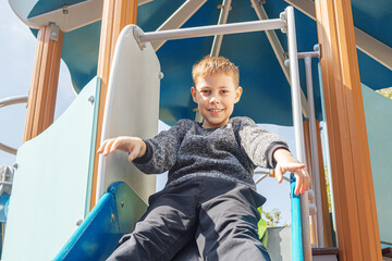 Happy Smiling Boy Sliding Down Blue Playground Slide at Outdoor Park Showing Pure Joy and Excitement During Active Playtime