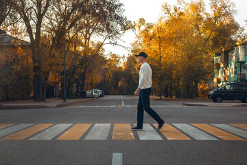Young Man Walking Across Urban Crosswalk During Golden Autumn Sunset, Peaceful City Street Scene...