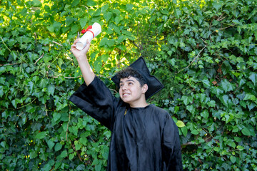 Young recent graduate boy, dressed in cap and gown, showing off his degree, celebrating