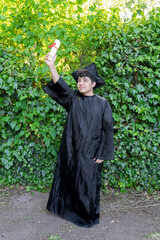 Young recent graduate boy, dressed in cap and gown, showing off his degree, celebrating