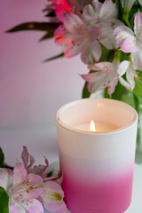 Burning candle surrounded by Peruvian lilies in a natural composition.