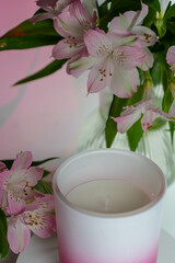 Pink vase and candle with Peruvian lilies in a glass vase.