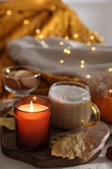 Burning candle, cocoa and dry leaves on table, closeup. Autumn atmosphere
