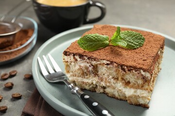 Piece of tasty tiramisu with fresh mint on grey table, closeup