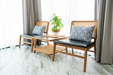 Plants in vase on wooden table and wooden soft chair with decorative cushion. perfect addition to light and airy living room in urban apartment
