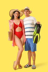 Happy young couple with flippers on yellow background