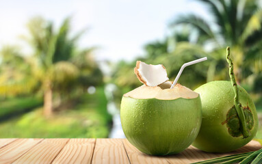 Cool coconut juice on wooden table with coconut tree background.