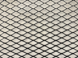 Industrial black expanded metal in diamond shape with light concrete background.