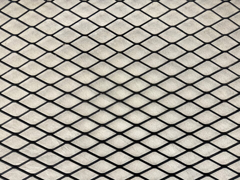 Industrial black expanded metal in diamond shape with light concrete background.