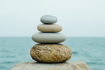 Emotional Balance. A serene stack of smooth stones balanced on a natural surface, overlooking a calm sea, evoking tranquility and harmony.