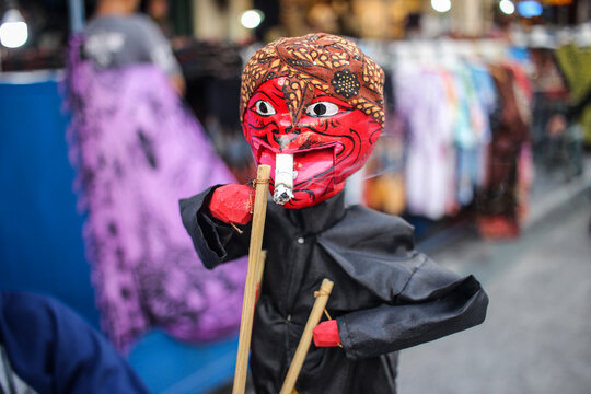 A vendor holding a traditional Cepot puppet, a vibrant character from Sundanese Wayang Golek. Ideal for themes of Indonesian culture, heritage, folk art, and traditional craftsmanship
