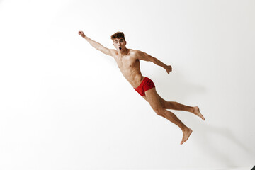 Obraz premium Energetic young man jumping in mid-air with an expressive face, showcasing excitement and joy against a white background. Concept of freedom and vitality.