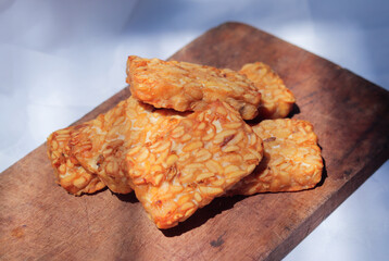 Golden-brown tempeh slices are arranged on a wooden board, showcasing their crispy texture and nutty flavor, perfect for a healthy snack or meal addition.