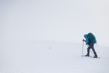 Climber in the mountains. A girl with a backpack and snowshoes walks through the snow.