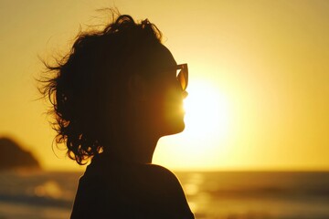 Golden charisma Concept. A silhouette of a person with curly hair wearing sunglasses against a vibrant sunset at the beach.