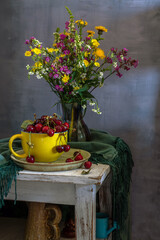 Still life with ripe cherries in a large yellow cup and a bouquet of meadow flowers.