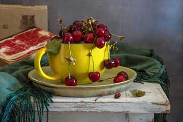 Still life with ripe and tasty cherries in a large yellow ceramic cup.