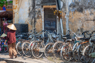 A woman in a conical hat walks past a row of parked bicycles, Hoi An, Vietnam